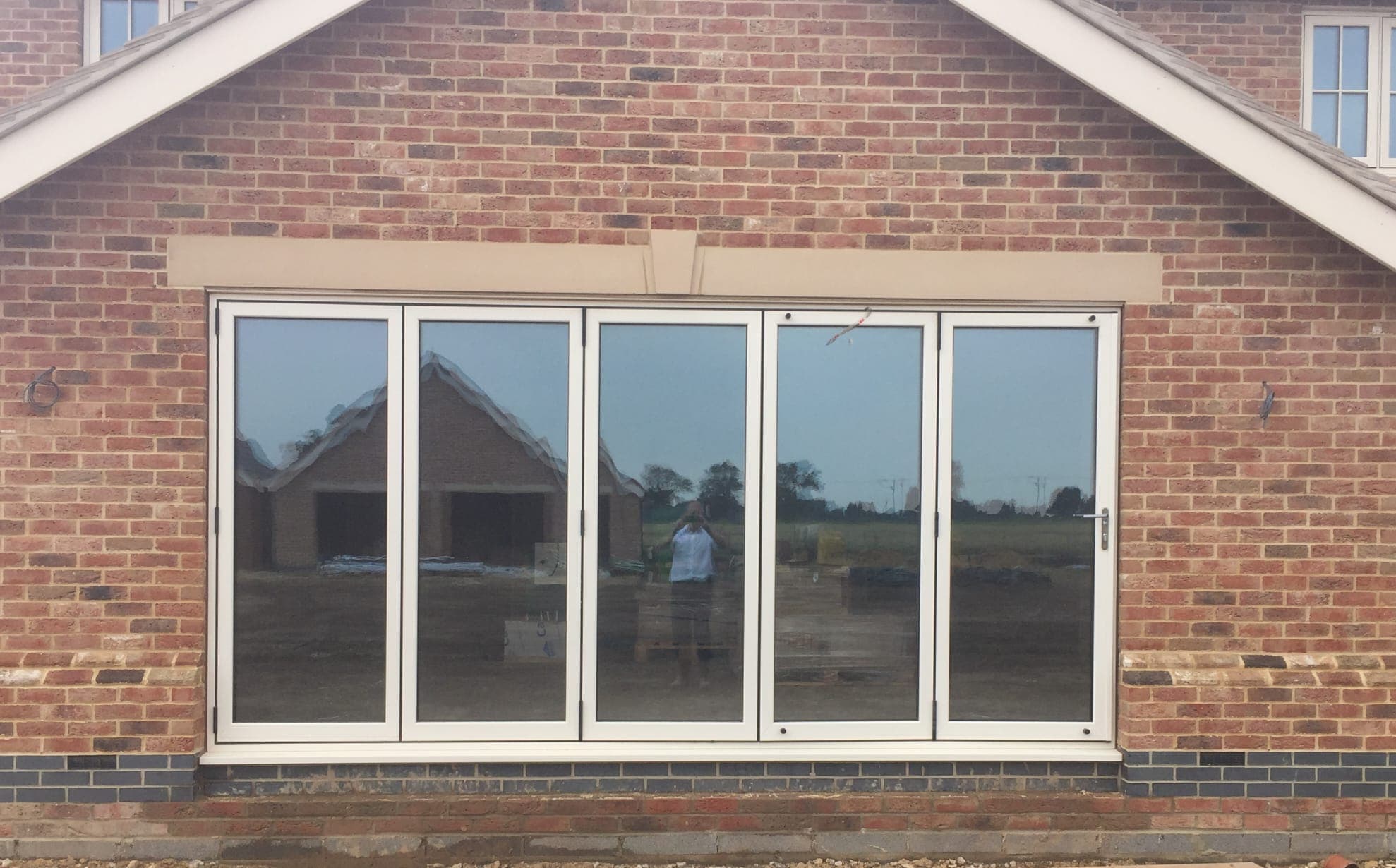 White five leaf bifolding doors in a red brick gable wall beneath a pale stone lintel