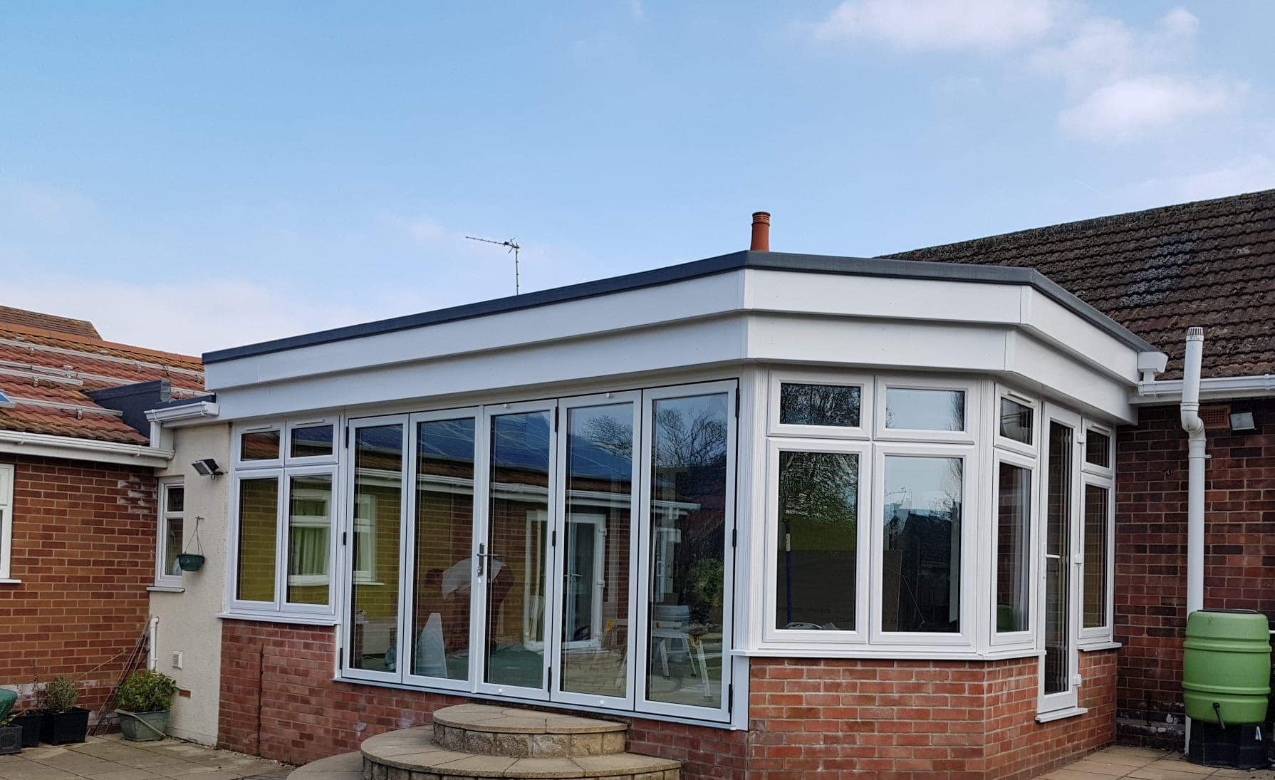 White five leaf bifolding doors in a flat roofed glazed room on a red brick dwarf wall