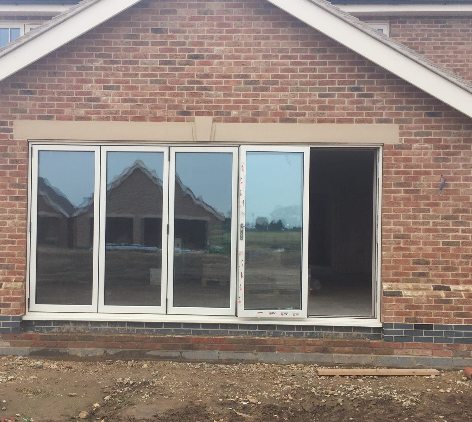 White bifolding doors with one leaf standing open in a red brick gable wall