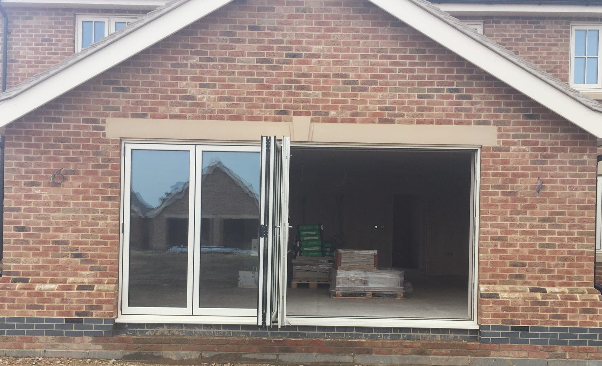 White bifolding doors part folded back into a stack of leaves in a brick gable