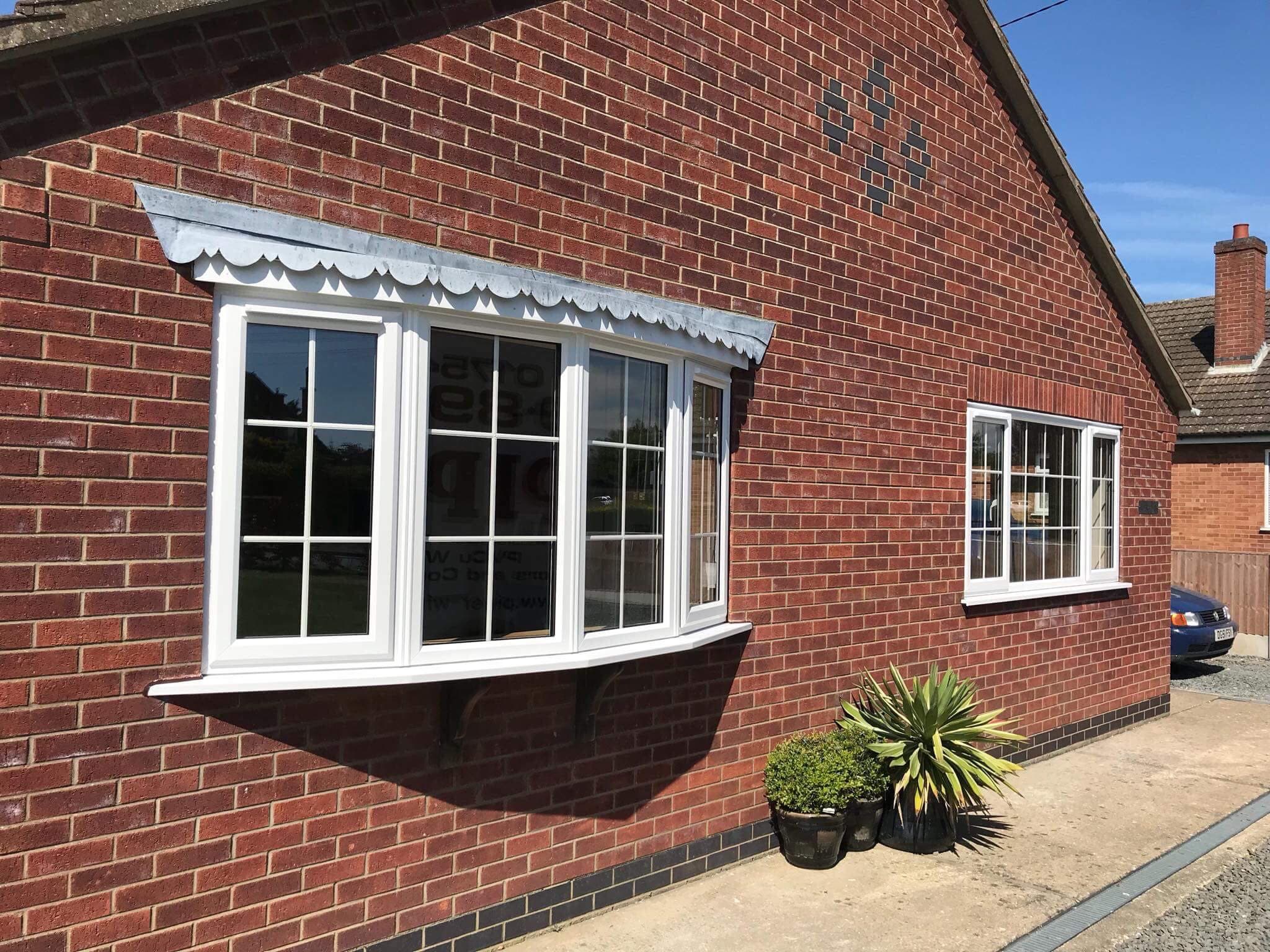 White bow window with Georgian glazing bars under a scalloped canopy, red brick bungalow