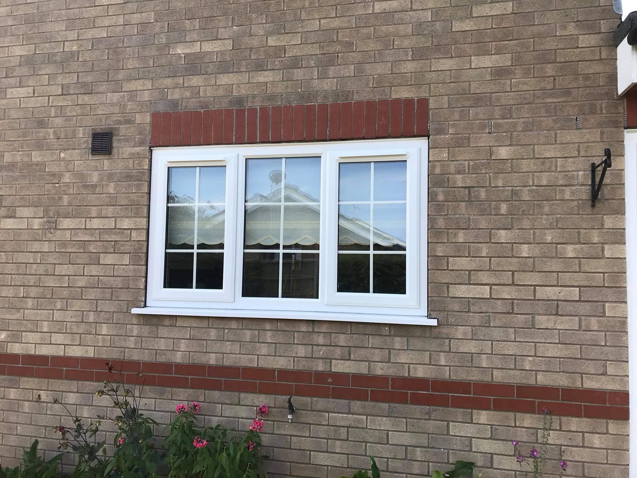 White three light casement window with Georgian glazing bars in a buff brick wall