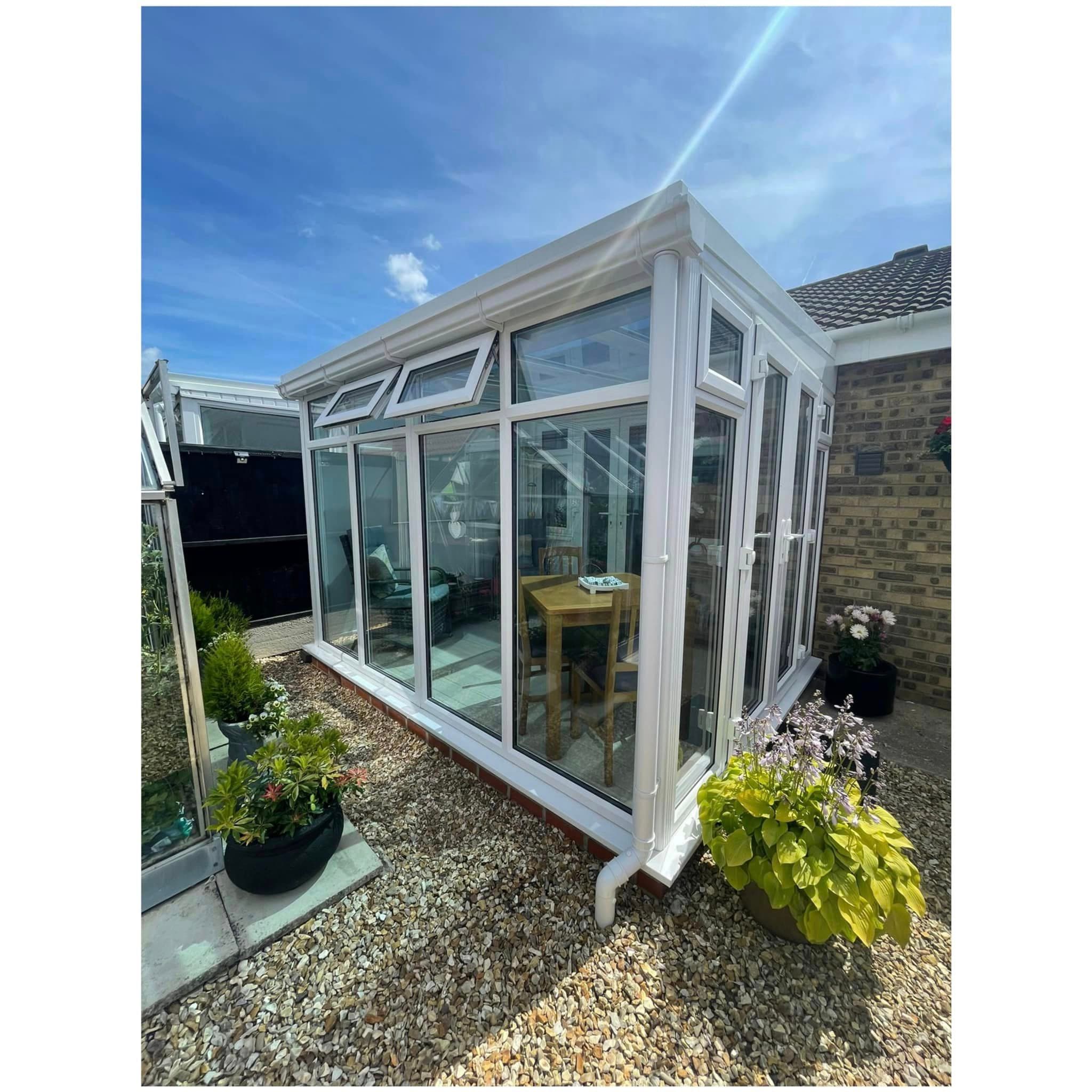 White conservatory with tall glazing and two top vents open beside a buff brick house