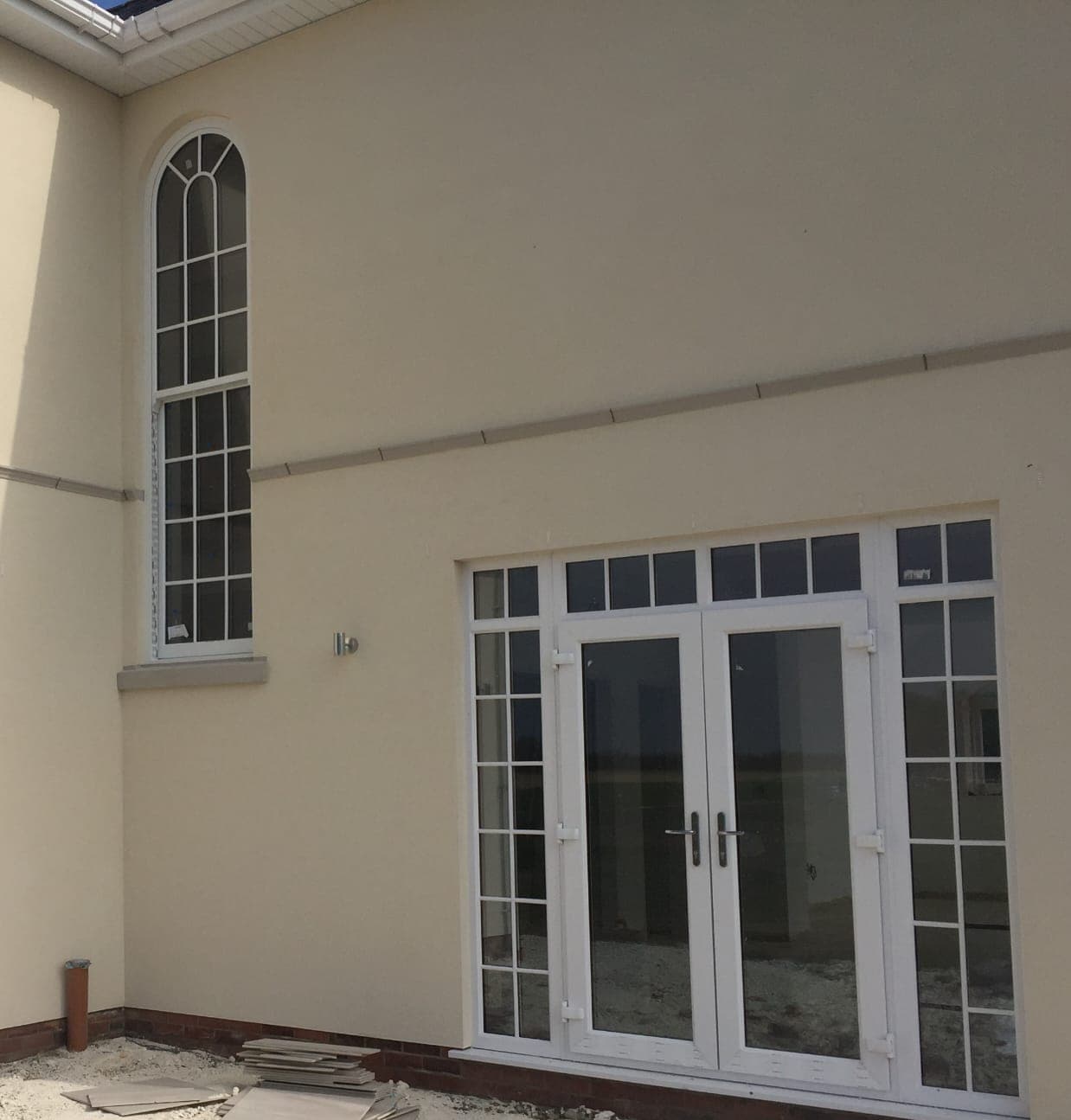 Tall white arched window with glazing bars beside white French doors with barred side panels