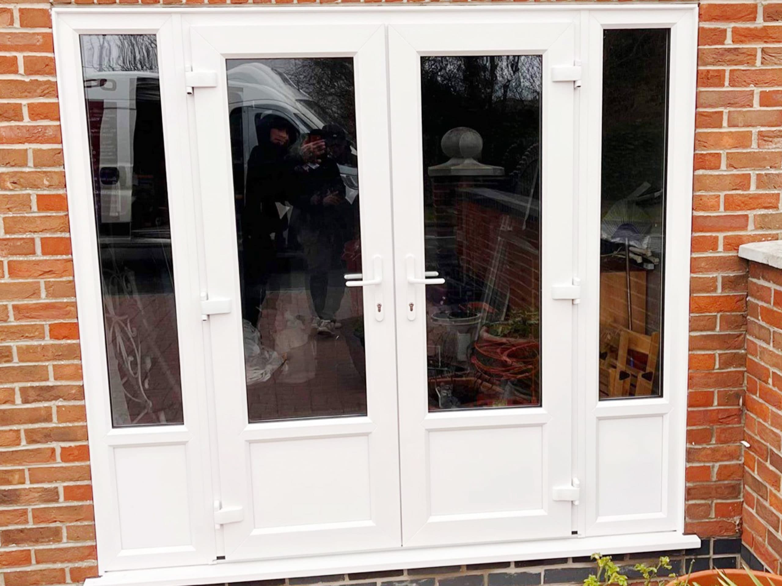 White french doors with matching glazed side panels in a red brick wall