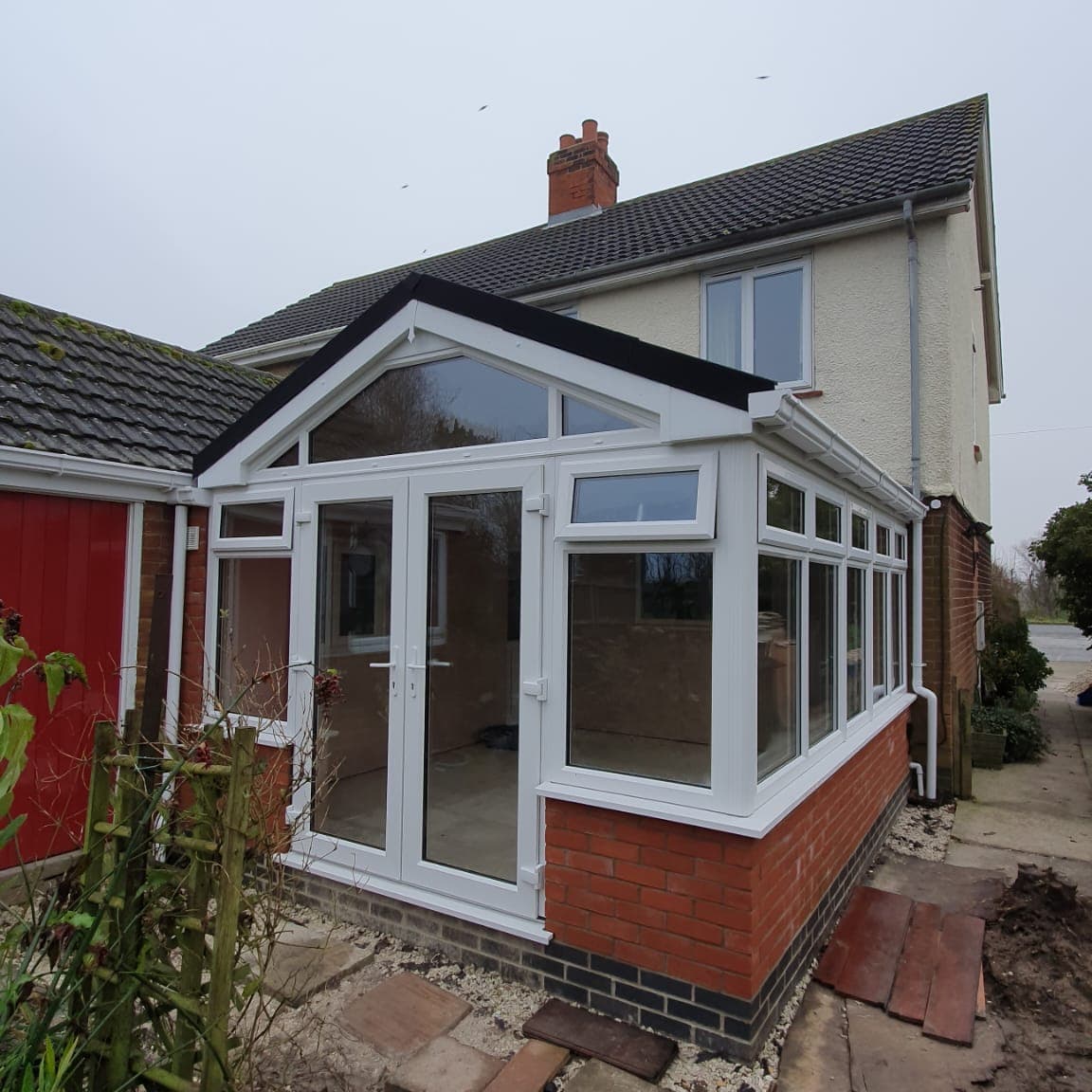 White gable fronted conservatory with French doors and a glazed gable on a brick dwarf wall