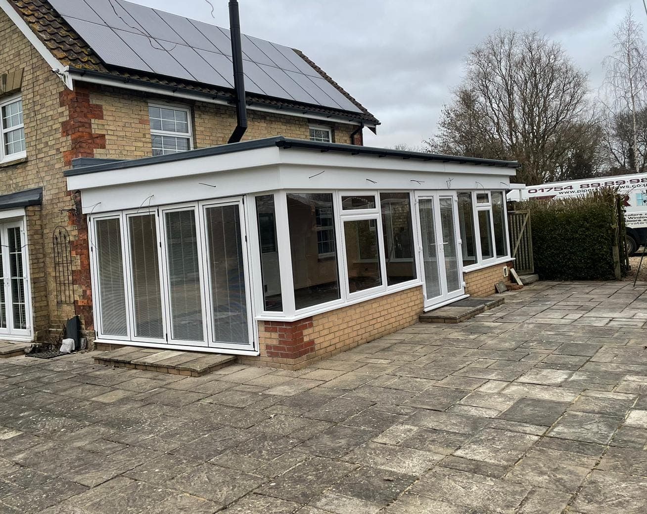 White glazed room with a flat roof, bifolding doors and French doors on a brick base