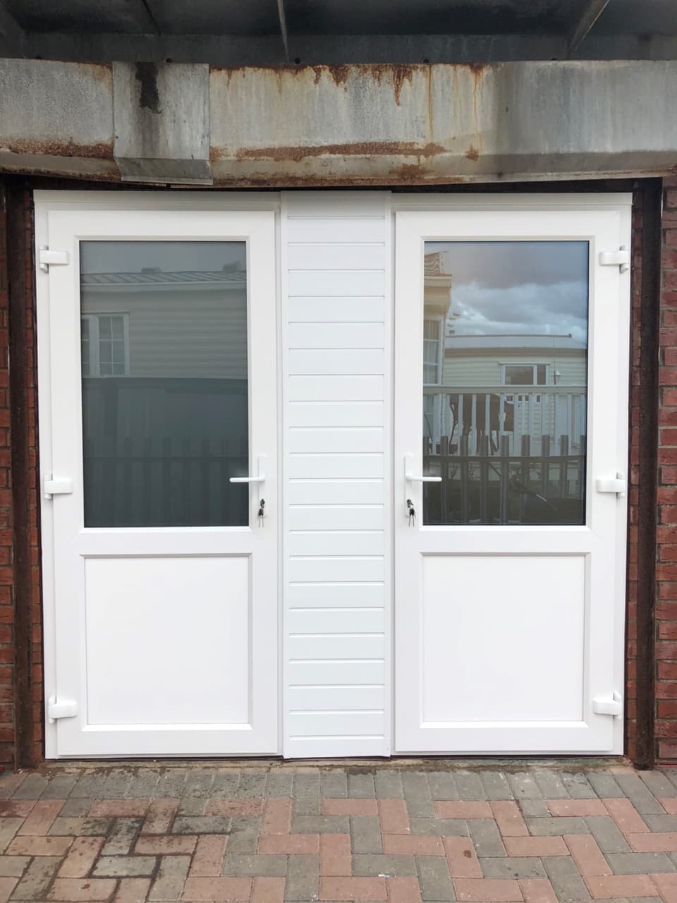 White half glazed doors either side of a boarded panel in a brick opening
