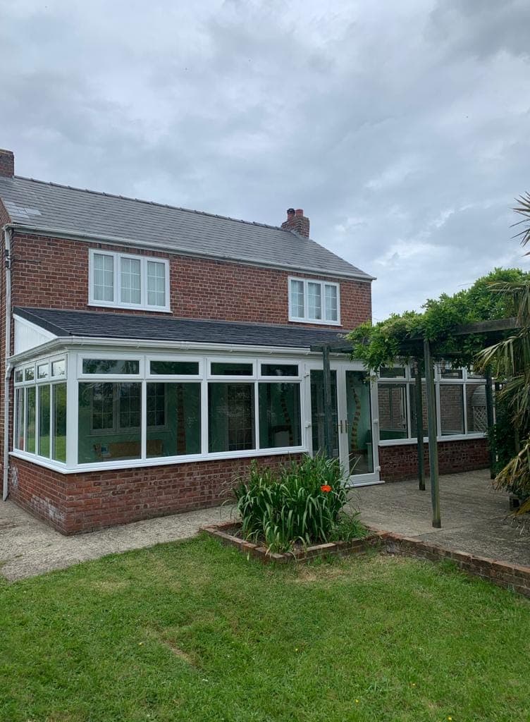 White lean to conservatory with a grey tiled roof and French doors on a brick dwarf wall