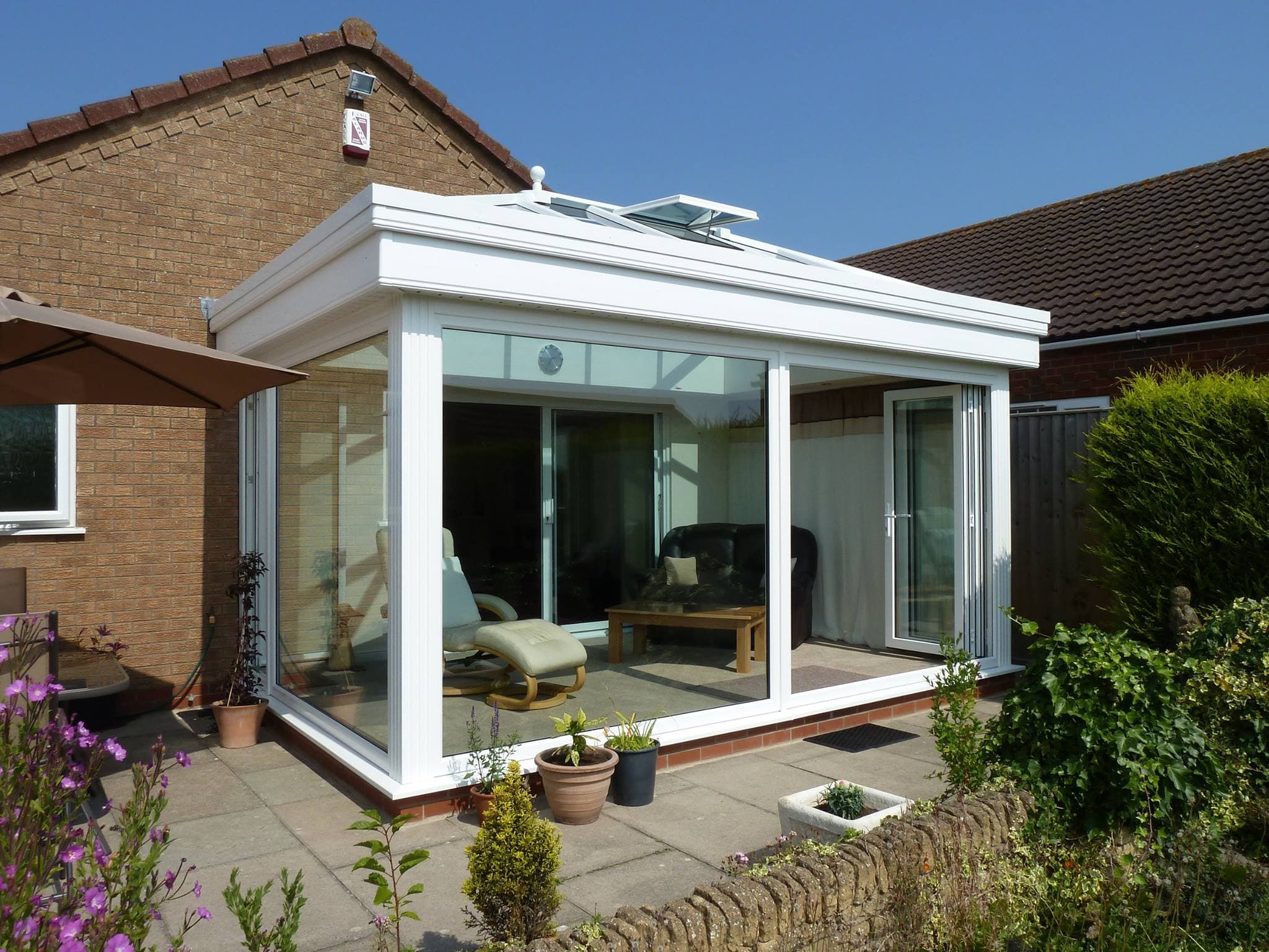 White framed orangery with a glazed roof lantern opening onto a paved patio