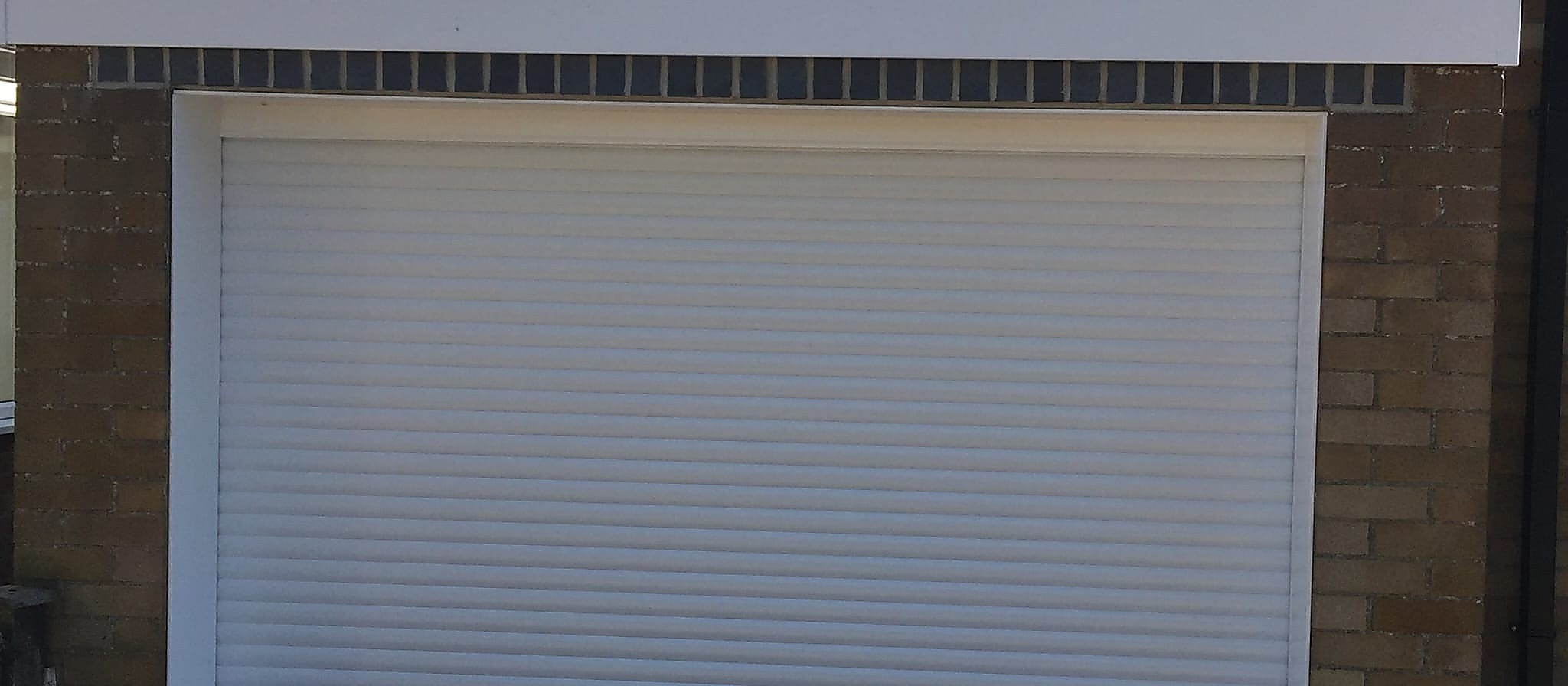 White roller garage door closed in its side guides on a flat roofed brick garage