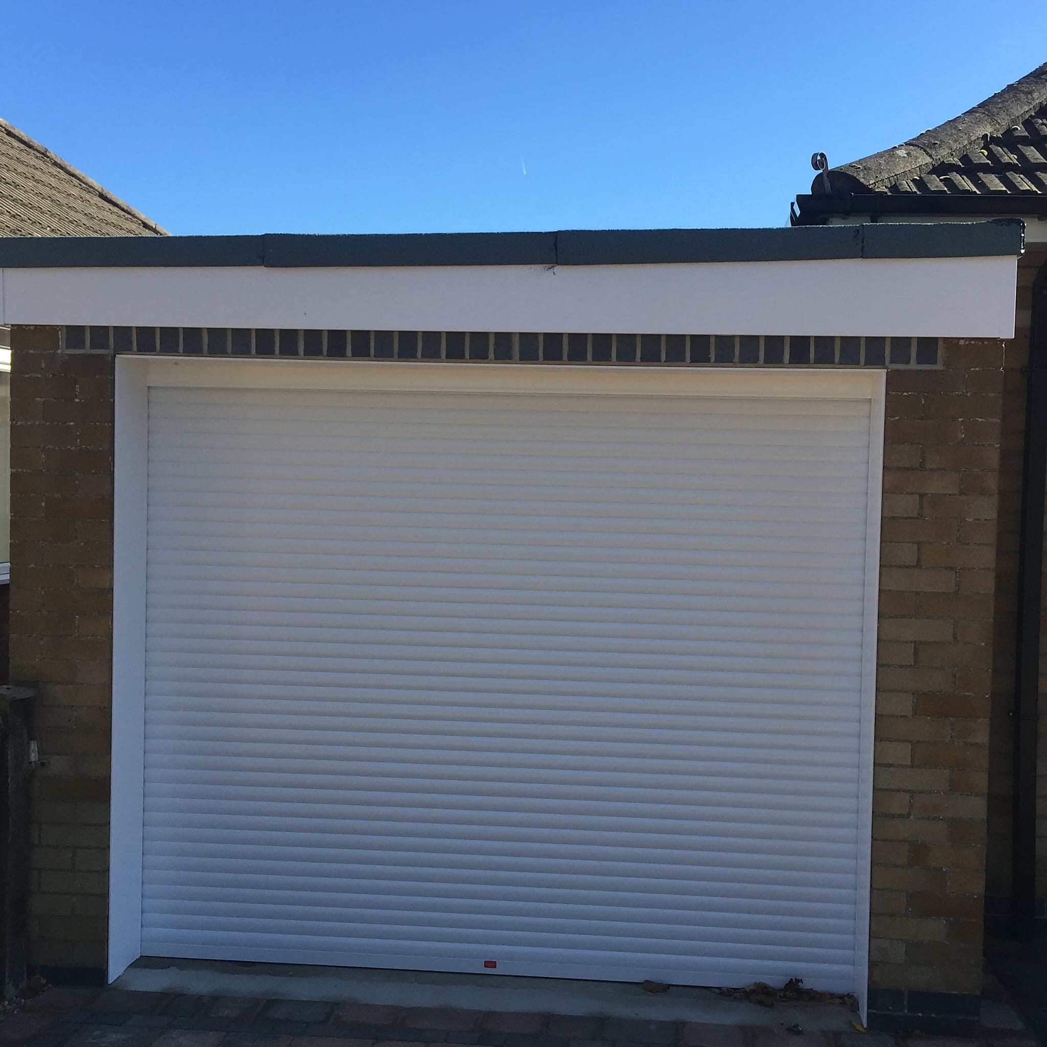White roller garage door closed in its side guides on a flat roofed brick garage