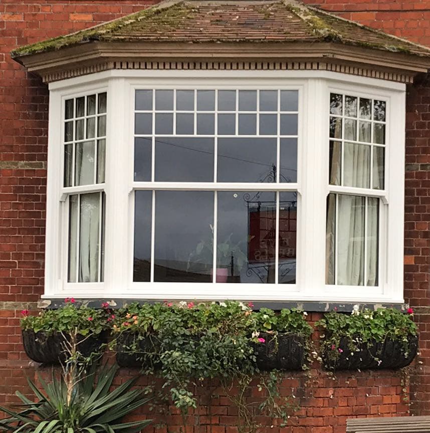 White sash windows with Georgian glazing bars fill a canted bay under a tiled roof