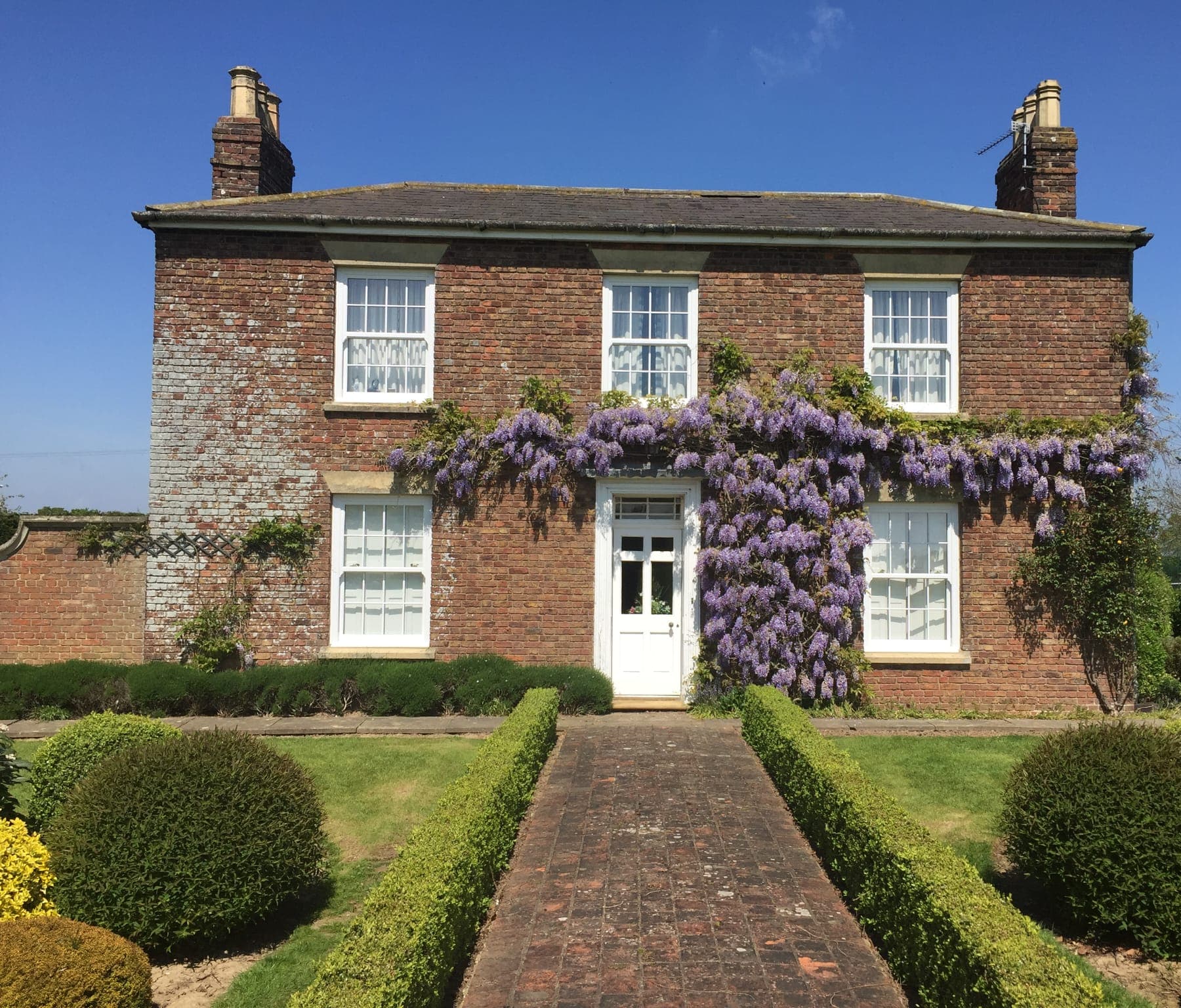 White sliding sash windows across the front of a red brick house with flowering wisteria