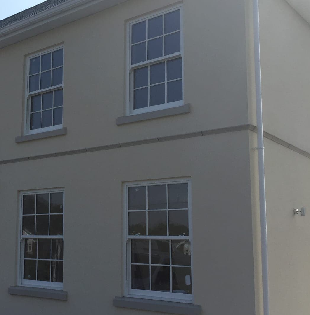 White sliding sash windows with Georgian glazing bars and grey stone sills on a cream rendered house